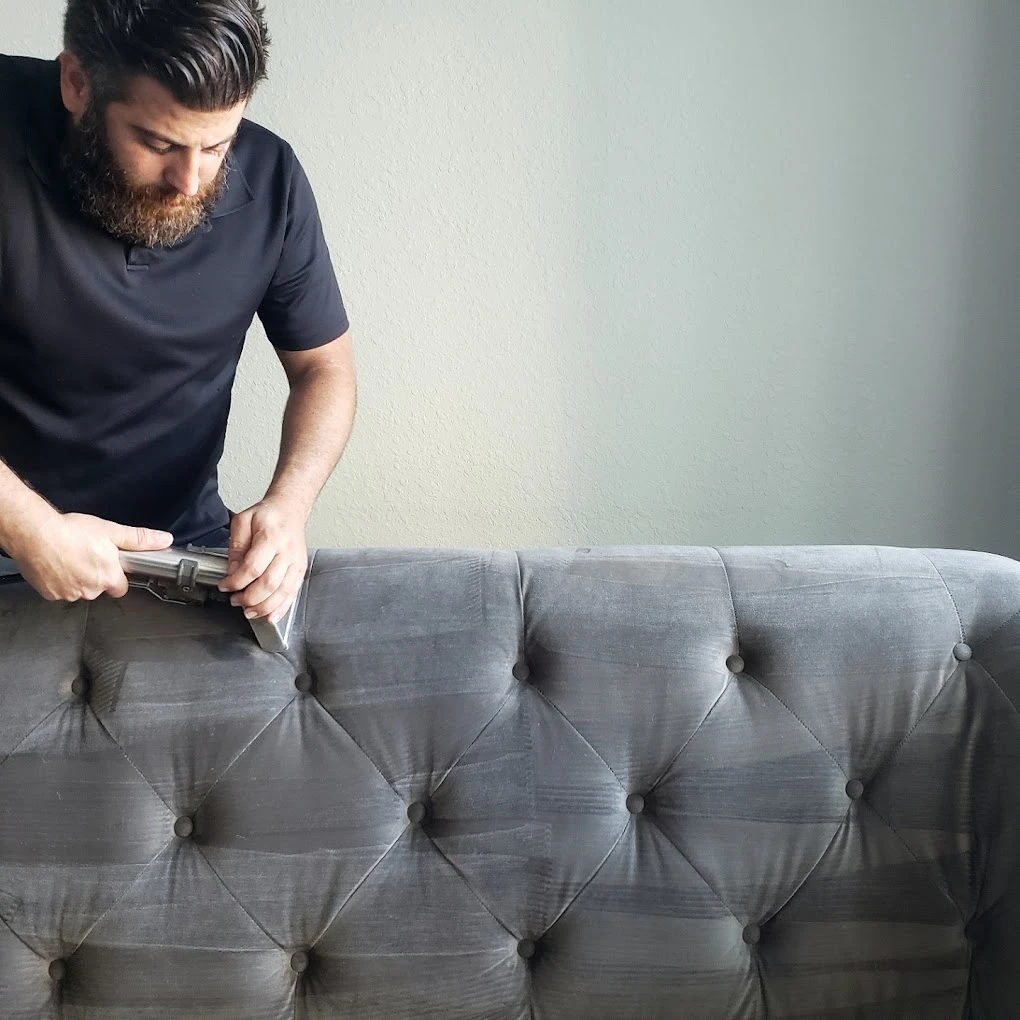 Steam tool cleaning a grey tufted sofa
